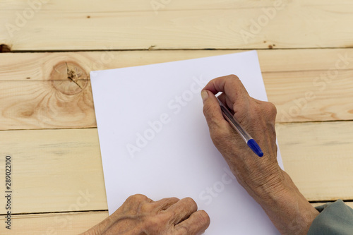 Hands of an elderly man are holding blank paper and a pen. Concept of testament, signing of an agreement, writing in old age. Image.