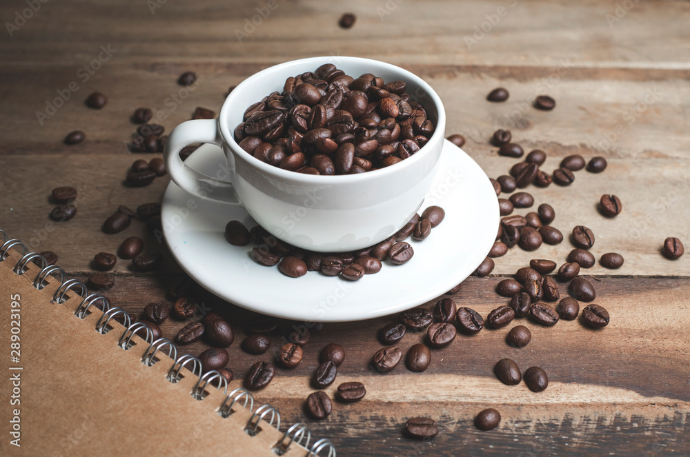 The coffee beans that are in the coffee mugs are laid on an old wooden table. The coffee beans that are in the coffee mugs are laid on an old wooden table.