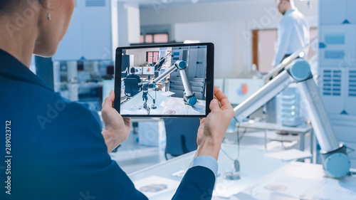 Female Industrial Robotics Engineer Uses Tablet Computer Recording a Video of Moving Robot Arm Used for Lifting, Moving Objects. Technology Research Facility for Machine Learning and Cloud Computing