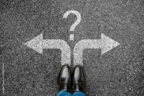 Top view of businessman black shoes standing on grunge concrete. Man feet with white question mark and left or right arrows sign on road background to future life. Choice concept of making decision.