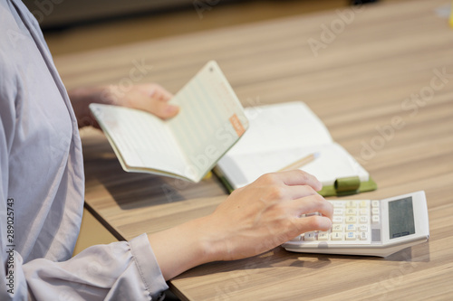 Foto 通帳をを見ながら電卓を打つ女性の手元