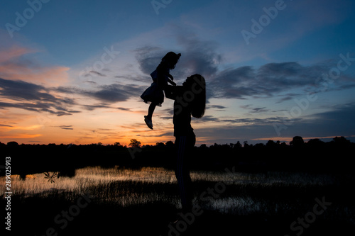 Silhouette woman throws up girl field in the evening. Concept to build relationships within the family.