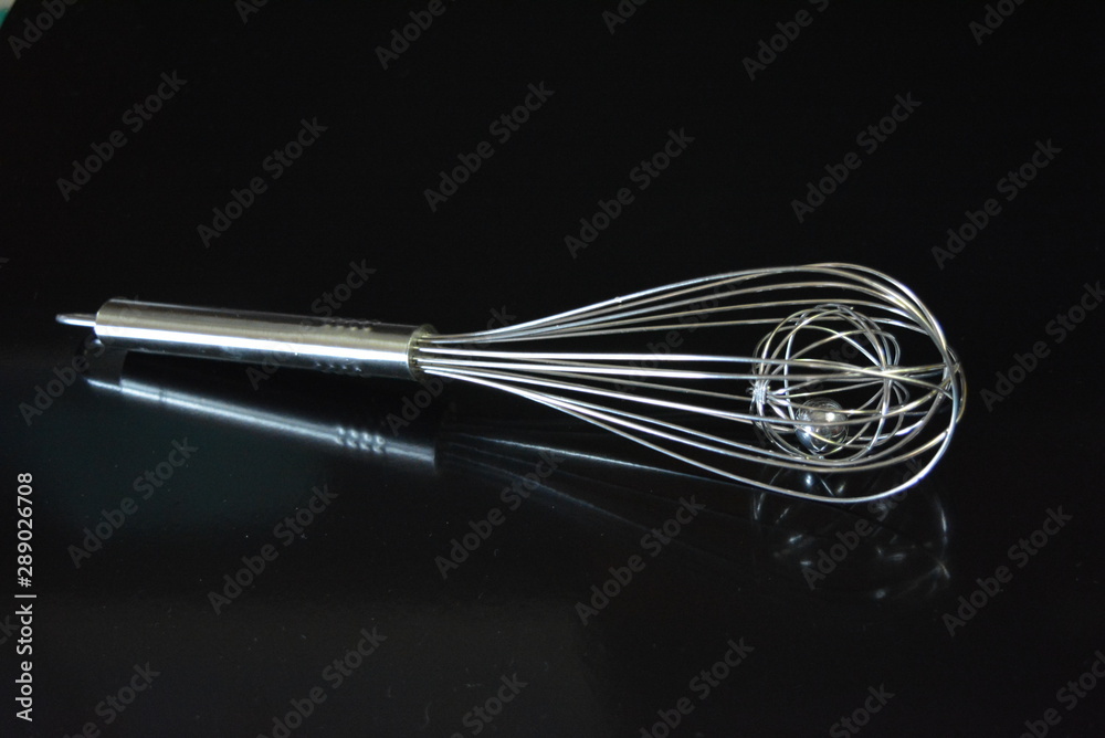 A beautiful metal whisk for whipping, stirring yolks and proteins, kitchen utensils for the kitchen are located on a black glossy surface. A beautiful metal whisk for whipping, stirring yolks and proteins, kitchen utensils for the kitchen are located on a black glossy surface.