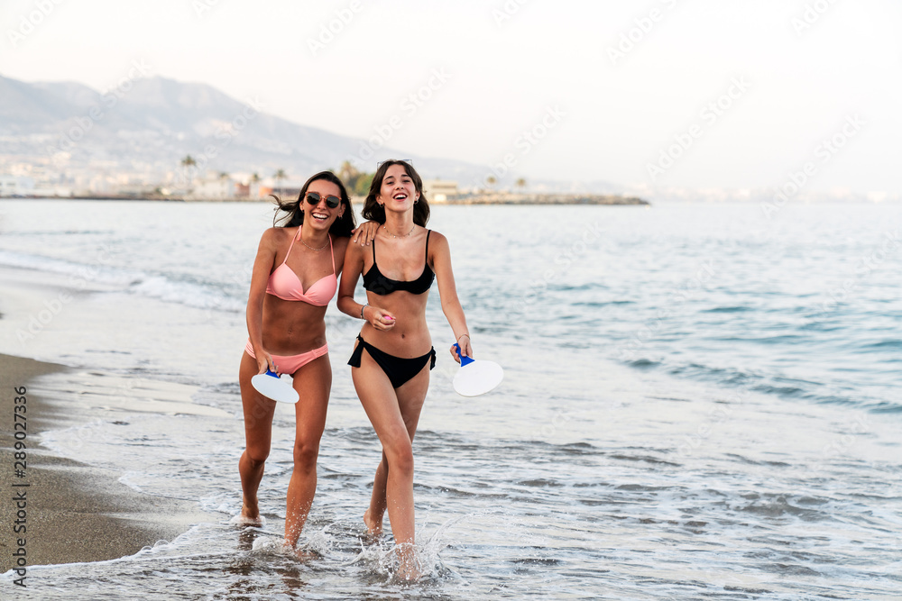 Girlfriends walking in embrace on foamy seashore Girlfriends walking in embrace on foamy seashore