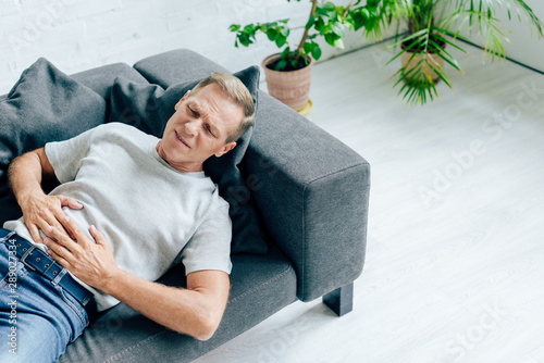 handsome man in t-shirt with stomachache lying on sofa photo