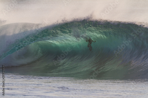 Huge green wave breaking on a shallow reef with a swimmer inside the wave