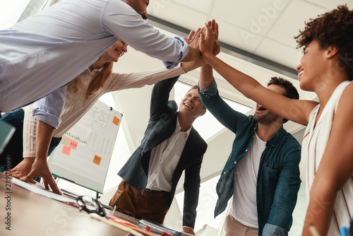 We did it Business people giving each other high-five and smiling while working together in the modern office