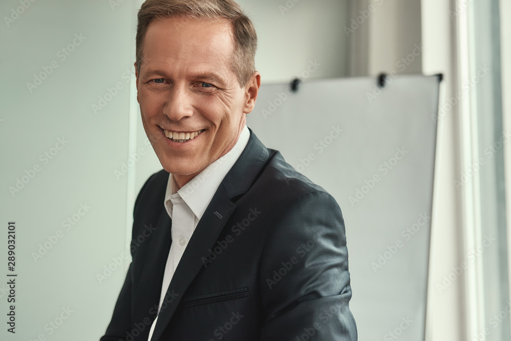Successful businessman. Handsome and cheerful mature man in formal wear looking at camera and smiling while sitting in the office Successful businessman. Handsome and cheerful mature man in formal wear looking at camera and smiling while sitting in the office