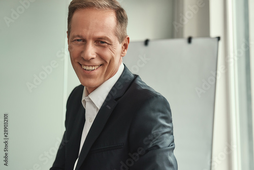 Successful businessman. Handsome and cheerful mature man in formal wear looking at camera and smiling while sitting in the office