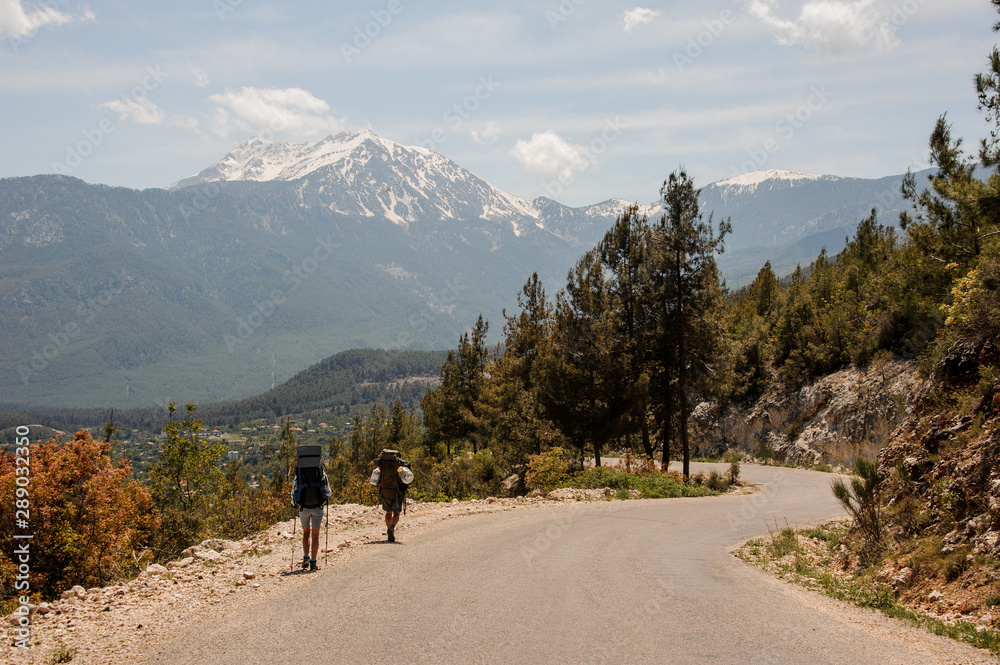 Two people walking on the road with hiking backpacks