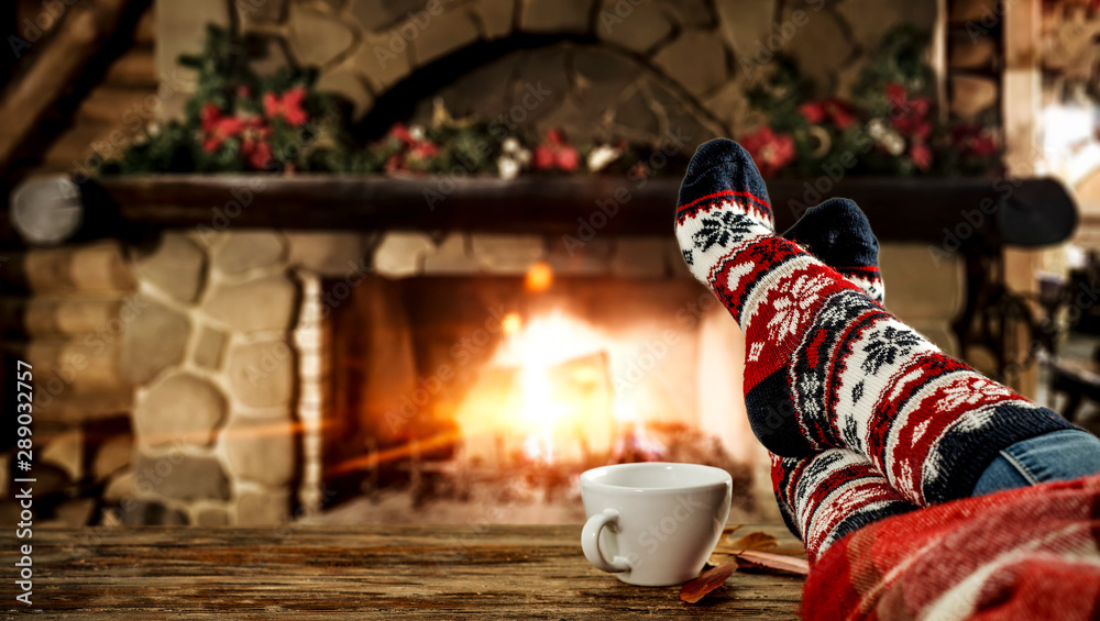 Woman legs with christmas socks and fireplace  - obrazy, fototapety, plakaty 