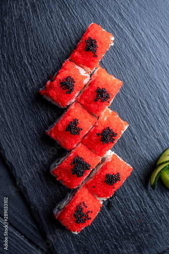 Set of sushi rolls with cream cheese, rice and salmon on a black board decorated with ginger and wassabi on a dark wooden background. Japanese cuisine. Food photo background. Top view photo