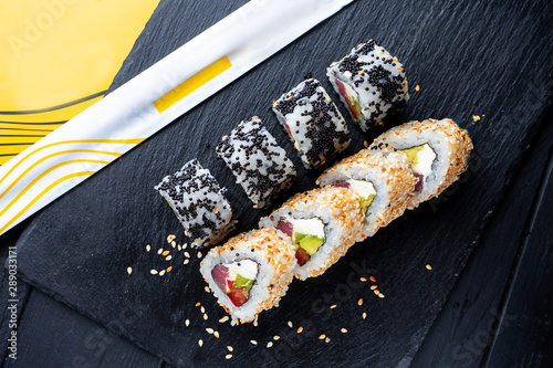 Set of sushi rolls with cream cheese, rice and salmon on a black board decorated with ginger and wassabi on a dark wooden background. Japanese cuisine. Food photo background photo