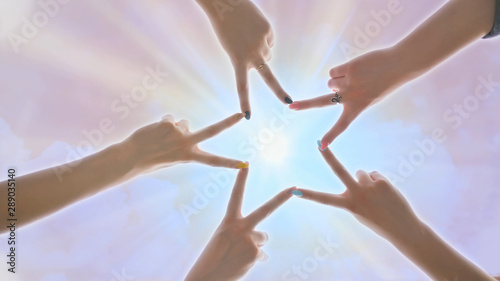 People forming star shape with their fingers against the backdrop of a pink magical sky with shining rays of the sun.