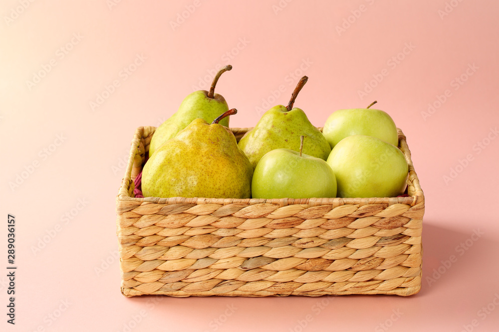Group of fresh, ripe and juicy apples and pears in a water hyacinth basket against pink background