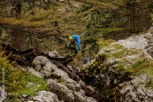 Girl in the raincoat walking on the rocks with hiking backpack and sticks