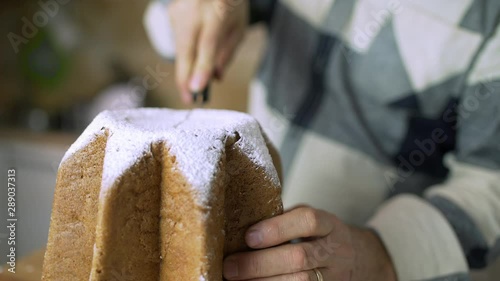 Man cutting a soft slice of an Italian Pandoro, a typical Christmas cake, and placing it on a wooden cutting board in the kitchen of home. Closeup of food.