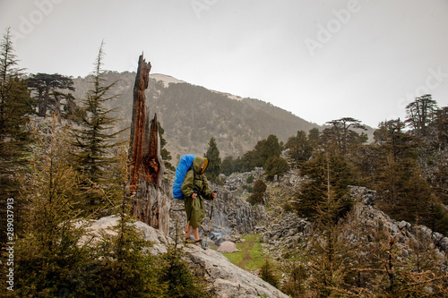 Girl in the raincoat with a hood walking up the rock with hiking backpack and sticks