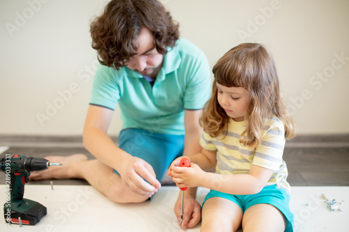 Father and his little daughter assembling furniture at home