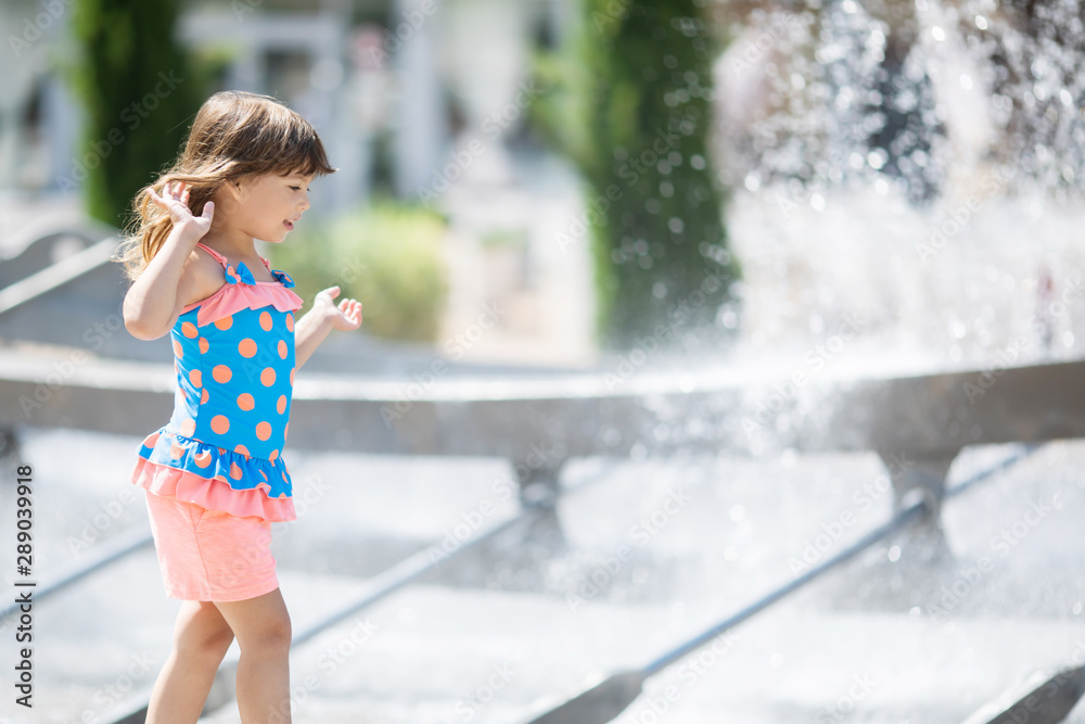 Naklejka premium Little adorable girl having fun in street fountain at hot sunny day