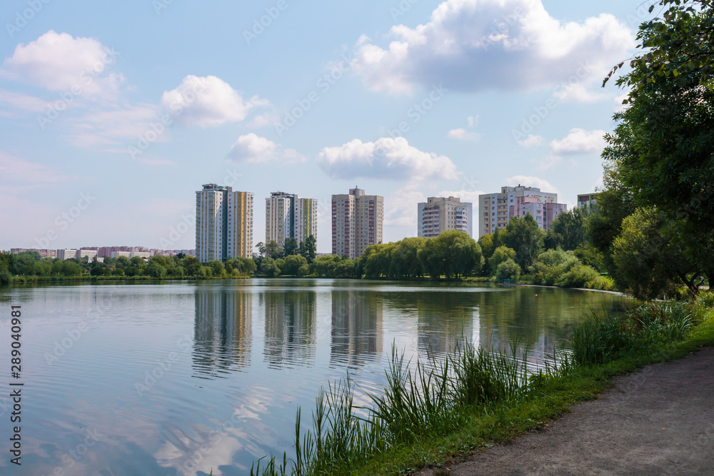the river flows on the background of the skyscraper reflected in the water and green trees and above them the blue sky with Cumulus clouds