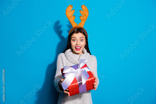 Petty lady with toy horns on her head giving red giftbox mommy wear knitted pullover isolated blue background