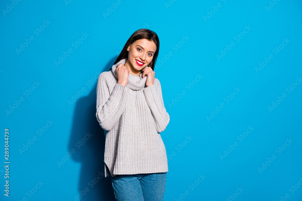 Portrait of pretty lady looking at camera with beaming smile touching her jumper isolated over blue background Portrait of pretty lady looking at camera with beaming smile touching her jumper isolated over blue background