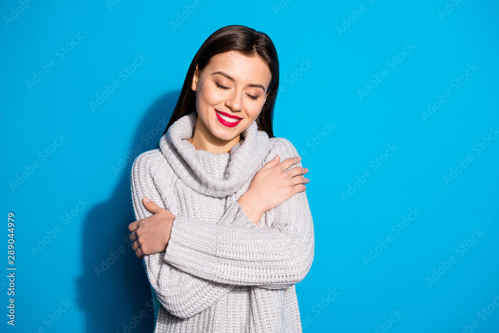 Portrait of positive woman cuddling herself with eyes closed wearing grey woolen pullover isolated over blue background Portrait of positive woman cuddling herself with eyes closed wearing grey woolen pullover isolated over blue background