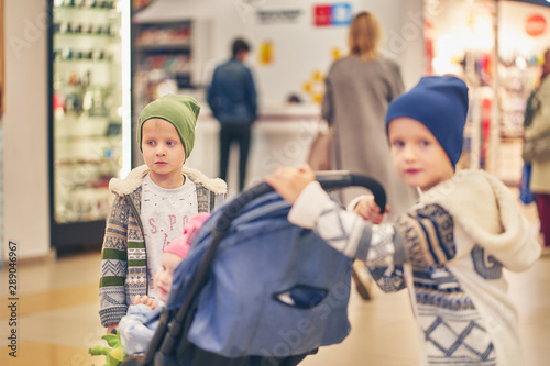 Two brothers with a little sister in a supermarket. they ride a pram while mom is shopping.