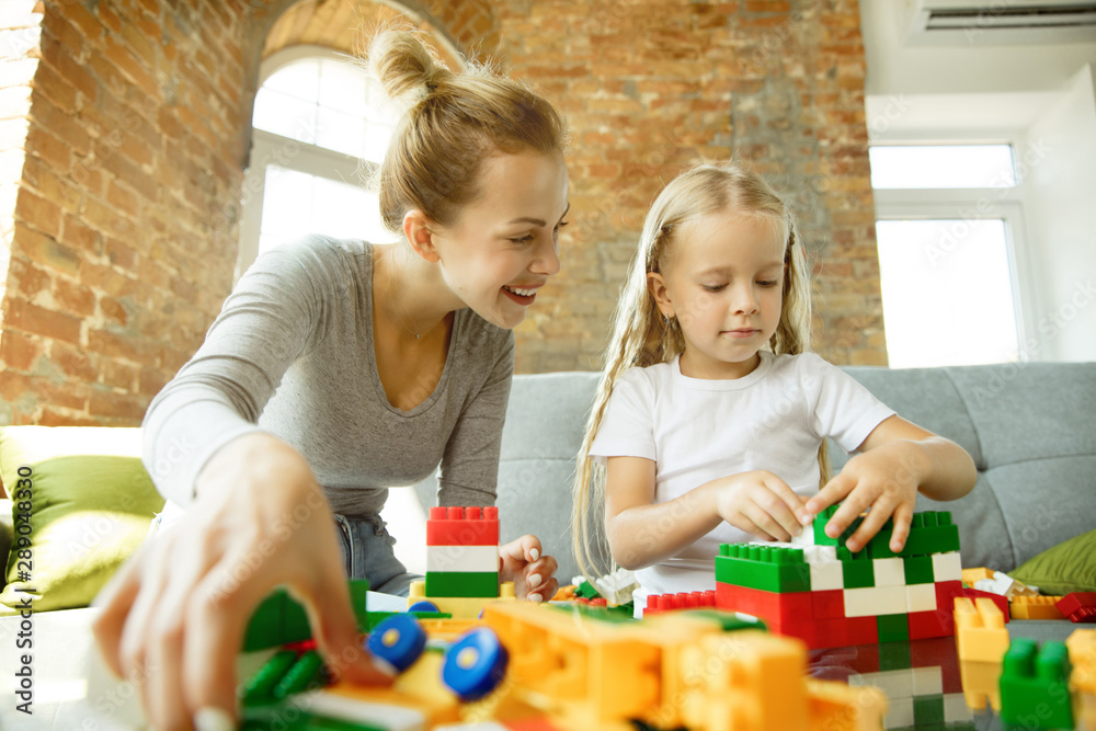 Fototapeta premium Kaukaski nauczycielka i mała dziewczynka lub mama i córka. Edukacja domowa. Siedzenie na sofie z plastikowym konstruktorem, nauka, rozmowa i zabawa. Edukacja, szkoła, koncepcja studiów.
