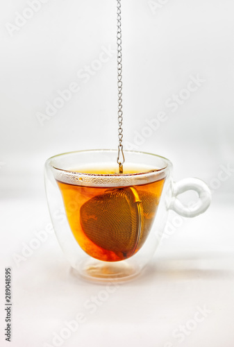 Tea strainer with tea leaves dropped in glass cup of boiling water photo