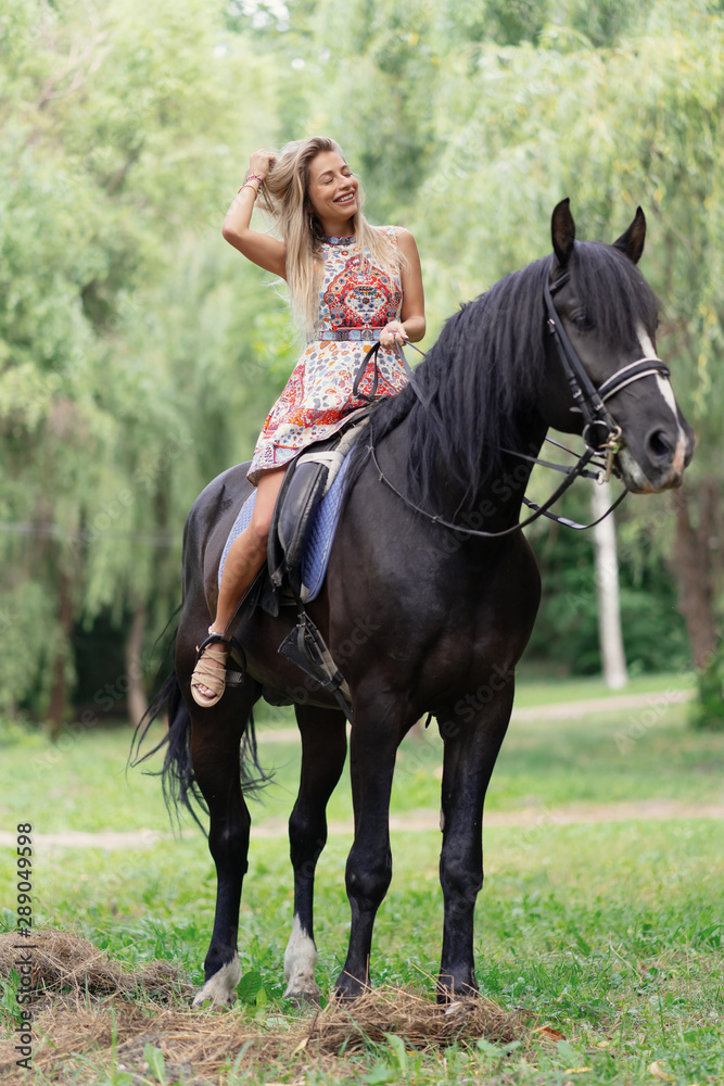 Young woman in a bright colorful dress riding a black horse Young woman in a bright colorful dress riding a black horse