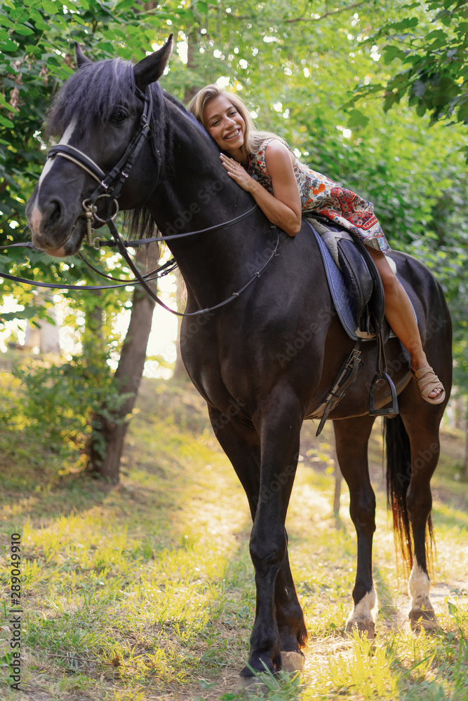 Young woman in a bright colorful dress riding a black horse Young woman in a bright colorful dress riding a black horse