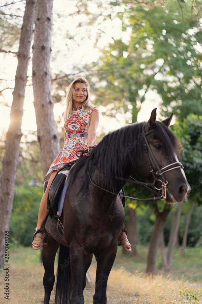 Young woman in a bright colorful dress riding a black horse Young woman in a bright colorful dress riding a black horse