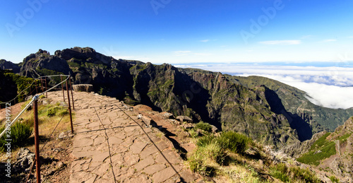 Wide angle shot of Mountain peaks against blue sky with a narrow passage along a ridge with high cliffs both sides. Pico do Areeiro to Pico Ruivo hiking trail, Madeira, Portugal, Europe