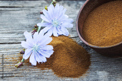 Blue chicory flower and a bowl of instant chicory powder on an old wooden table. Chicory powder. The concept of healthy eating a drink.