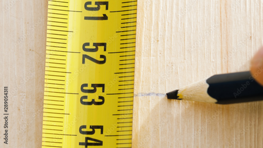 Closeup of hands of unrecognizable man using pencil and putting mark on wood plank holding measuring tape Closeup of hands of unrecognizable man using pencil and putting mark on wood plank holding measuring tape