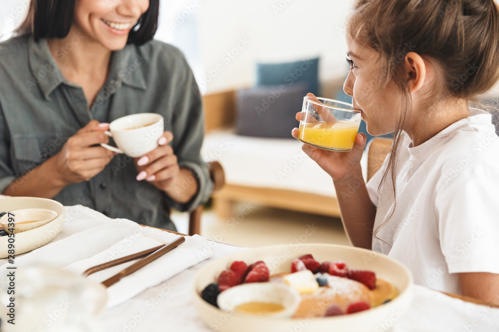 Image of smiling family mother and little daughter having breakfast at home in morning