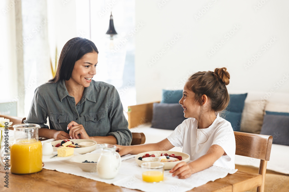 Image of positive family mother and little daughter having breakfast at home in morning