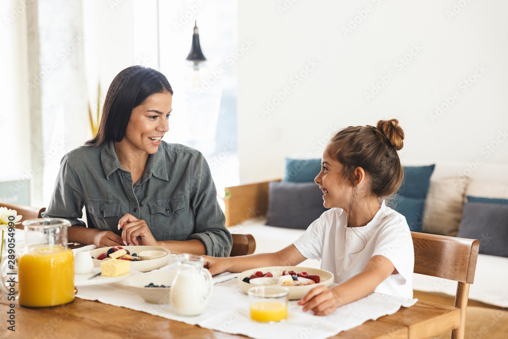 Image of positive family mother and little daughter having breakfast at home in morning Image of positive family mother and little daughter having breakfast at home in morning