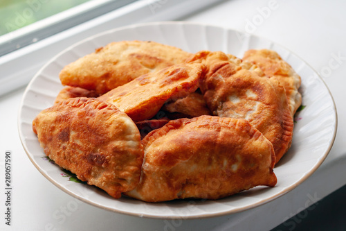 Chebureks. Appetizing homemade pasties in a plate on the windowsill.