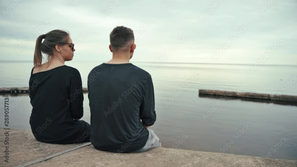 Couple sitting at the beach. Young man and woman in love sitting, on a cloudy summer day. Couple sitting at the beach. Young man and woman in love sitting, on a cloudy summer day.