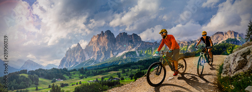 Couple cycling on electric bike, rides mountain trail. Woman and Man riding on bikes in Dolomites mountains landscape. Cycling e-mtb enduro trail track. Outdoor sport activity. photo