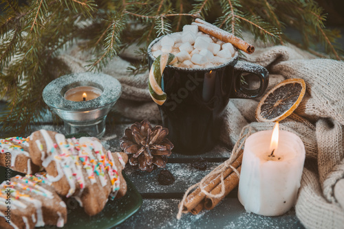 1 mug with hot chocolate and marshmallows, cinnamon stick and Lollipop, candle, spruce branch on a dark background, cone, cookies, knitted fabric