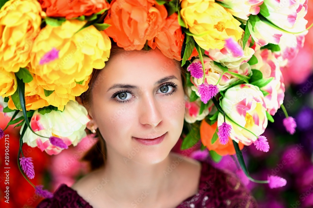 A large portrait of a pretty girl with a floral wreath on her head on a colorful background. Smiles, happiness, beauty.