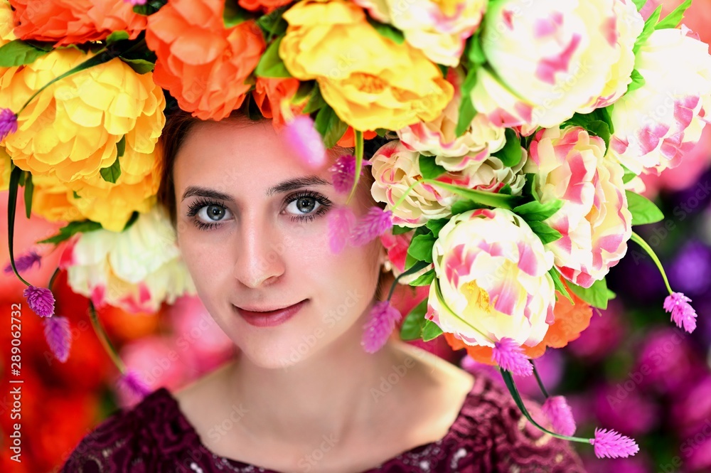 A large portrait of a pretty girl with a floral wreath on her head on a colorful background. Smiles, happiness, beauty.
