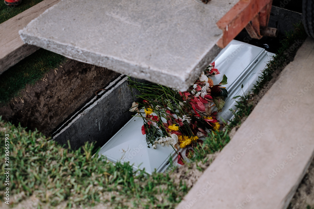 Cement slab was lowered to cover the coffin. Casket of the dead, with flowers from family and