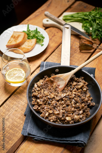 Stewed mushrooms in pan with toasts and parsley on wooden table