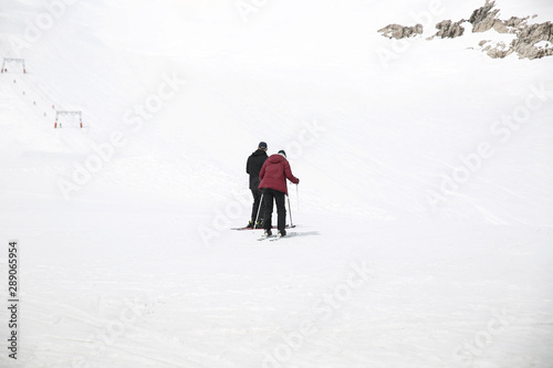 Two people skiing on a snow-covered mountain and a ski lift is in the background