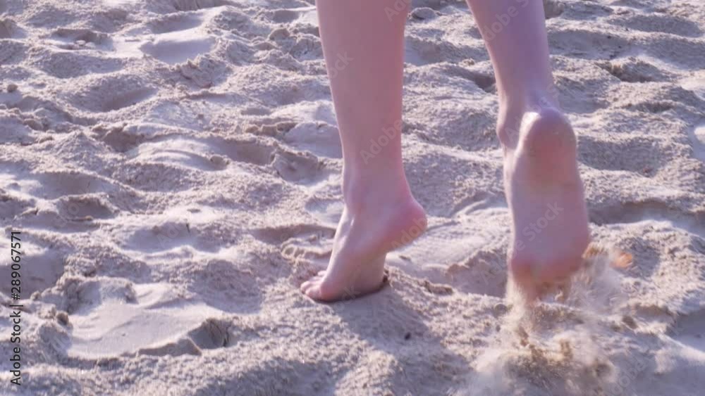 Rear view of female feet close up. Girl walking barefoot on tiptoes and turning around on sand at sunset in slow motion Rear view of female feet close up. Girl walking barefoot on tiptoes and turning around on sand at sunset in slow motion